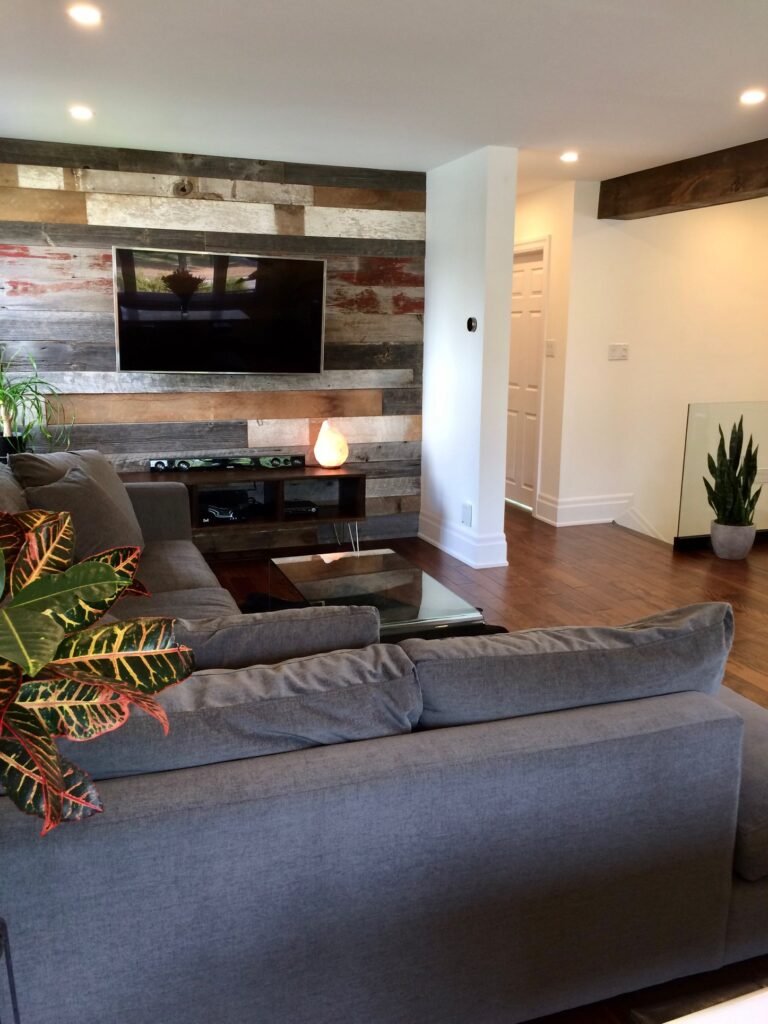 Modern living room renovation by HB Renovations featuring a reclaimed wood accent wall, wall-mounted TV, hardwood flooring, and contemporary furniture design.
